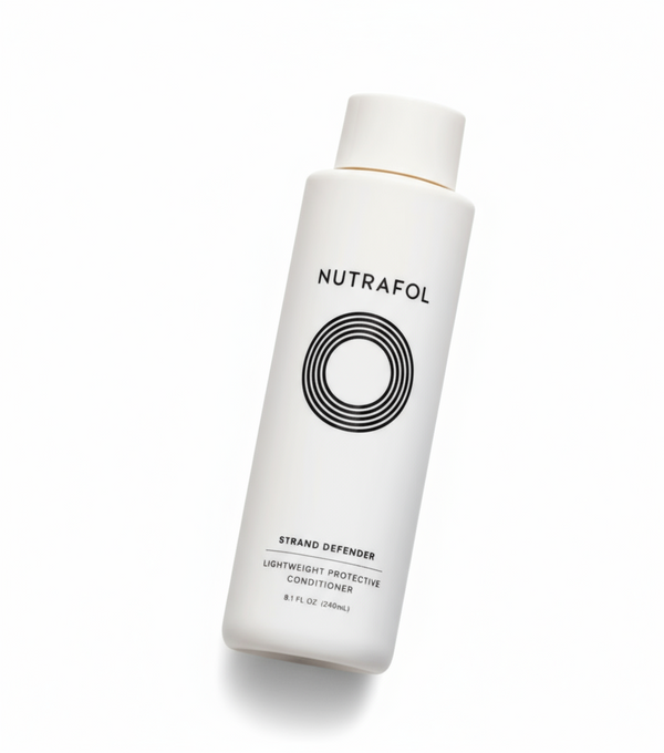 A hand holding a bottle of Nutrafol Strand Defender conditioner, which is designed to strengthen hair and defend against damage.